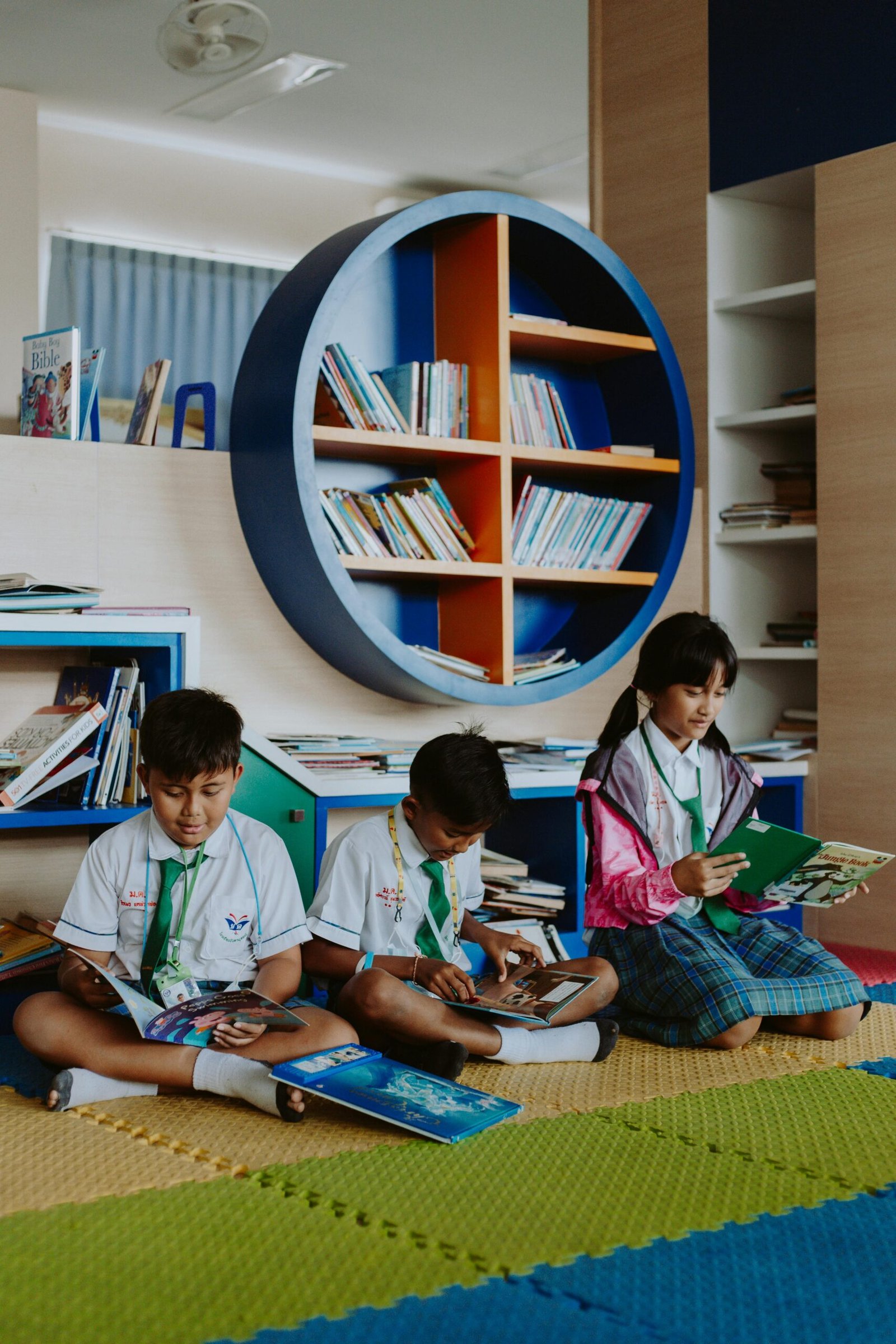 Children in school uniforms enjoy reading books in a modern library with colorful shelves.