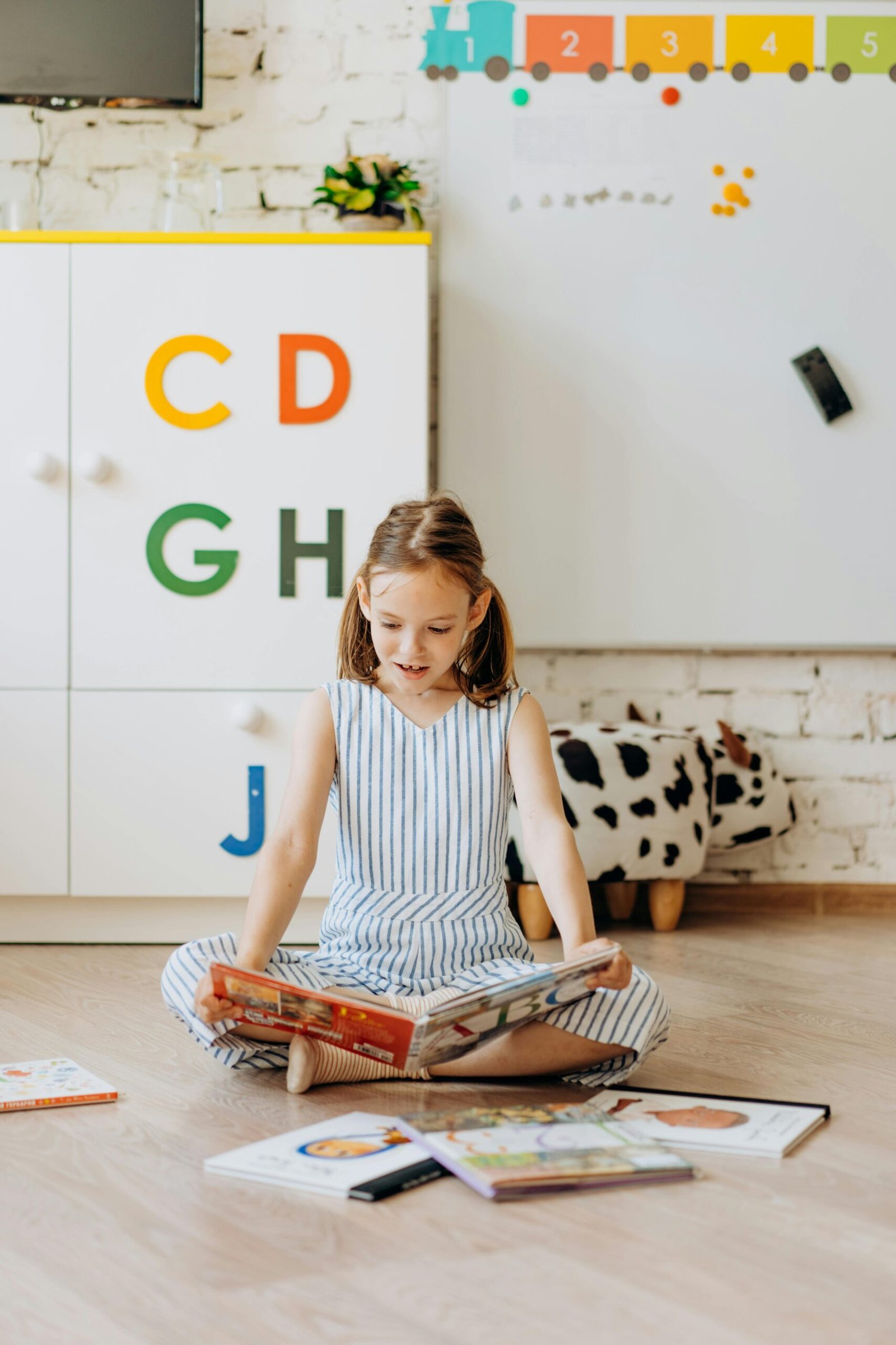 Young girl reading a book surrounded by educational decor indoors.