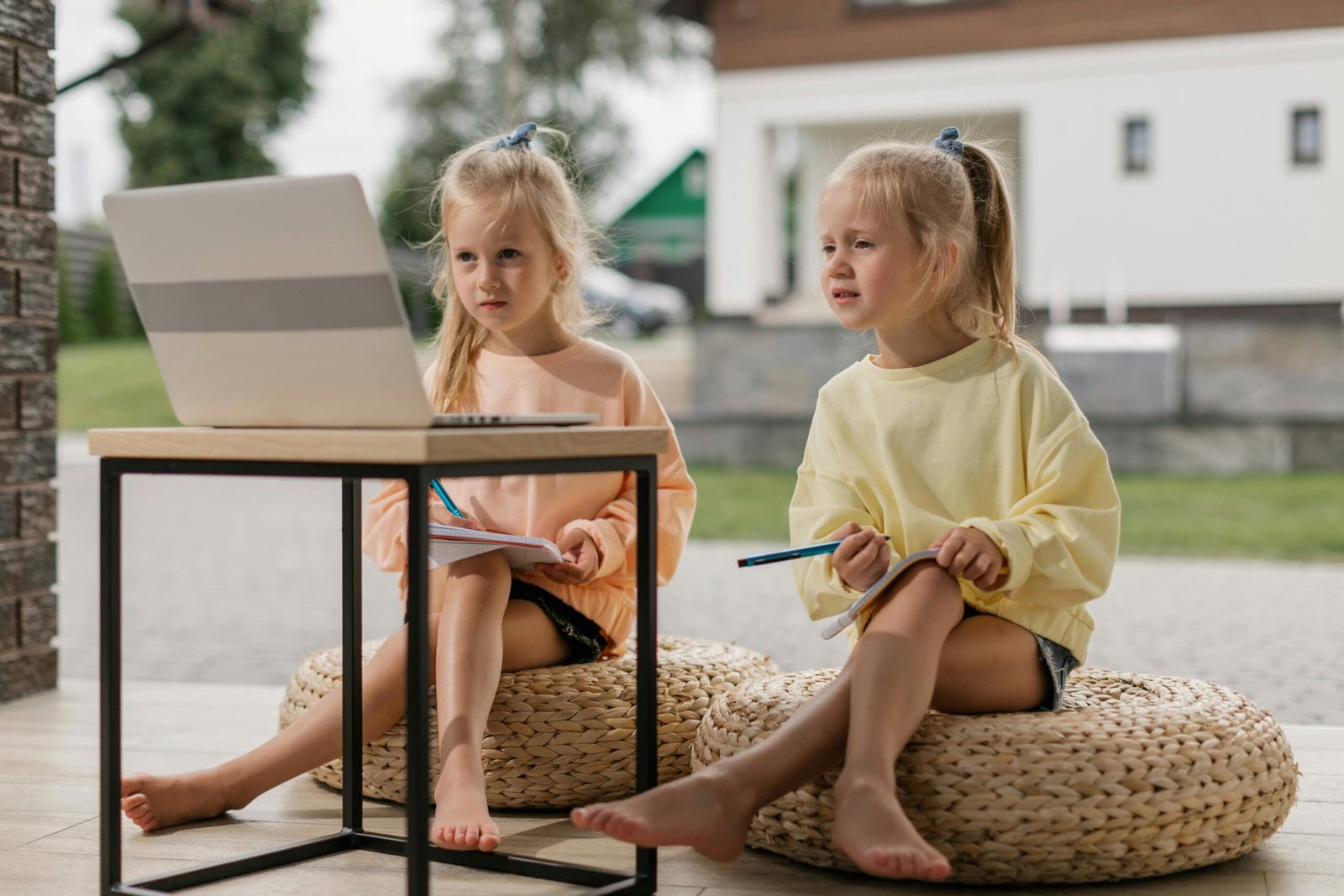 Twin girls studying online with a laptop outdoors, engaging in distance learning during the day.